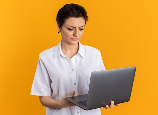 Frowning middle-aged woman holding and looking at laptop
