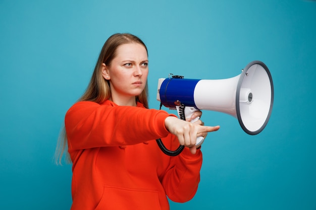 Frowning young blonde woman holding speaker looking and pointing at side 