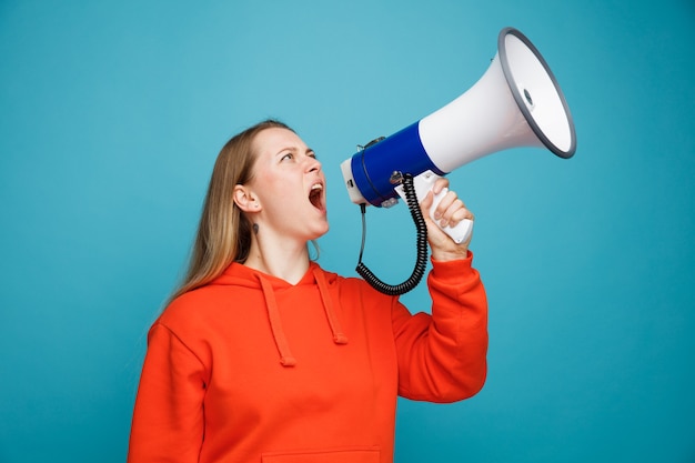 Frowning young blonde woman looking up shouting in loud speaker 