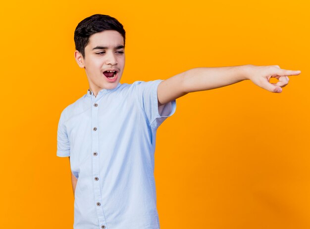 Frowning young caucasian boy looking and pointing at side isolated on orange background