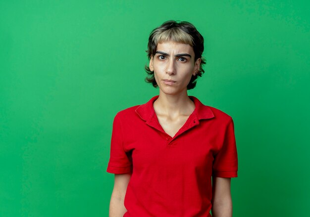 Frowning young caucasian girl with pixie haircut standing and looking at camera isolated on green background with copy space