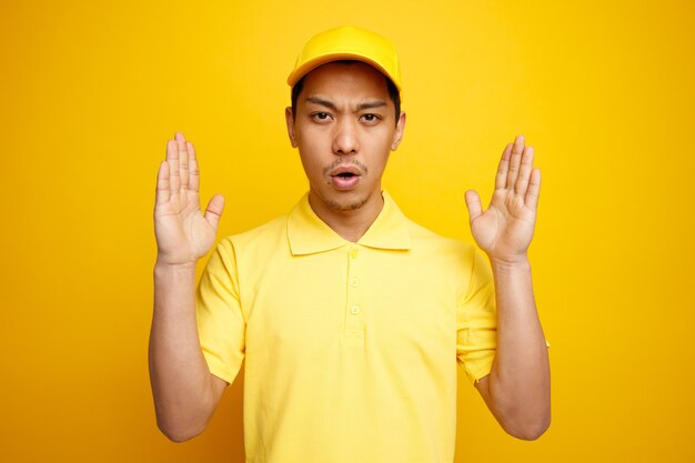 Frowning young delivery man wearing cap and uniform doing size gesture 