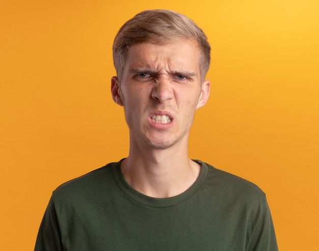 Frowning  young handsome guy wearing green shirt isolated on yellow wall