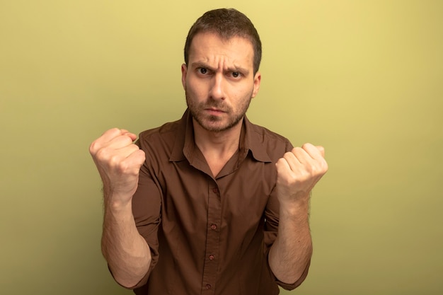 Frowning young man looking at front doing be strong gesture isolated on olive green wall