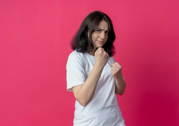 Frowning young pretty caucasian girl doing boxing gesture at camera isolated on crimson background with copy space