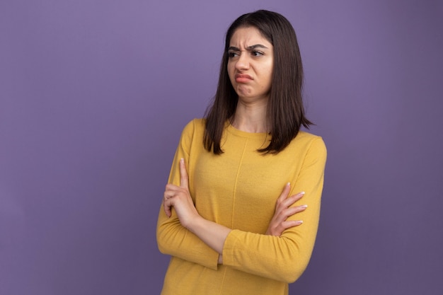 Frowning young pretty caucasian girl standing with closed posture looking at side isolated on purple wall with copy space