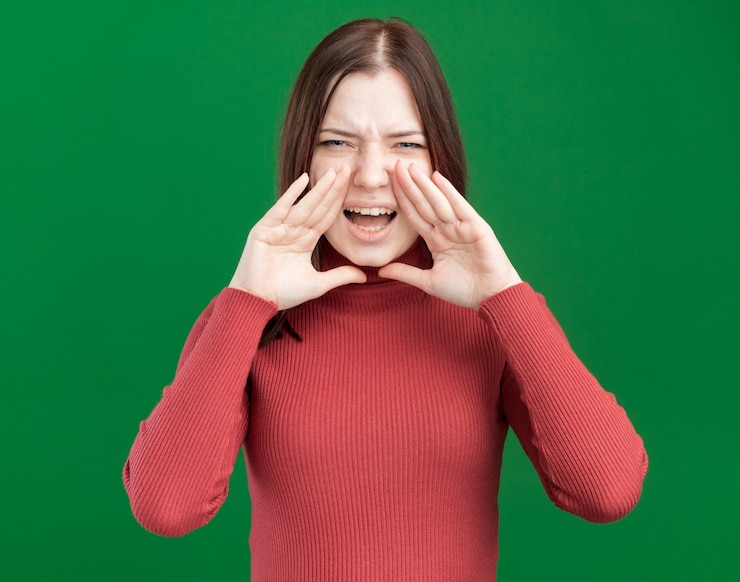 免費 Photo 眉毛<unk>的年轻漂亮的女人把手靠近嘴巴看着前面大声呼叫一个人孤立在绿色墙上