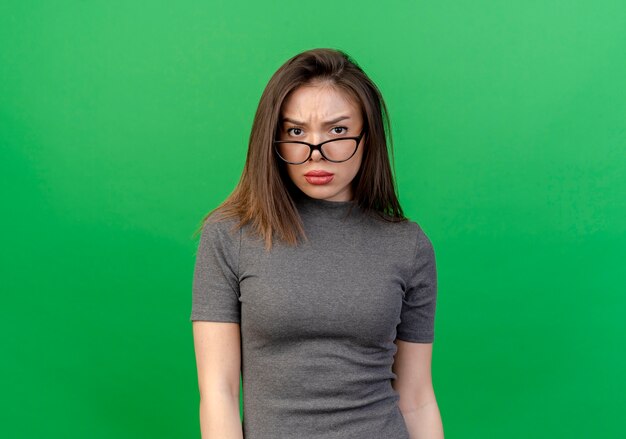 コピースペースで緑の背景に分離された眼鏡をかけて眉をひそめている若いきれいな女性