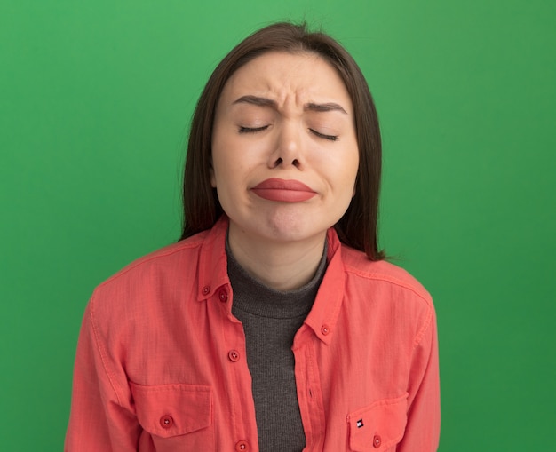 Frowning young pretty woman with closed eyes isolated on green wall