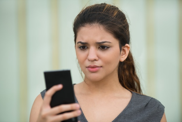 Frowning young woman reading message on cellphone