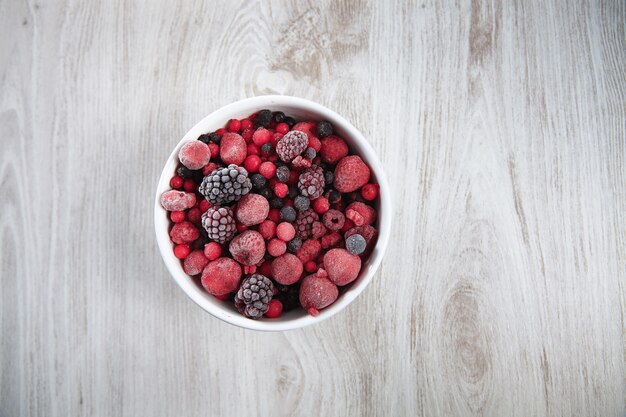 Frozen berries, black currant, red currant, raspberry, blueberry. top view in a vintage ceramic white bowl on rustic wooden table isolated