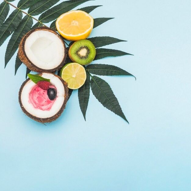 Frozen ice cream inside the halved coconut; orange; kiwi and lemon on leaves against blue background