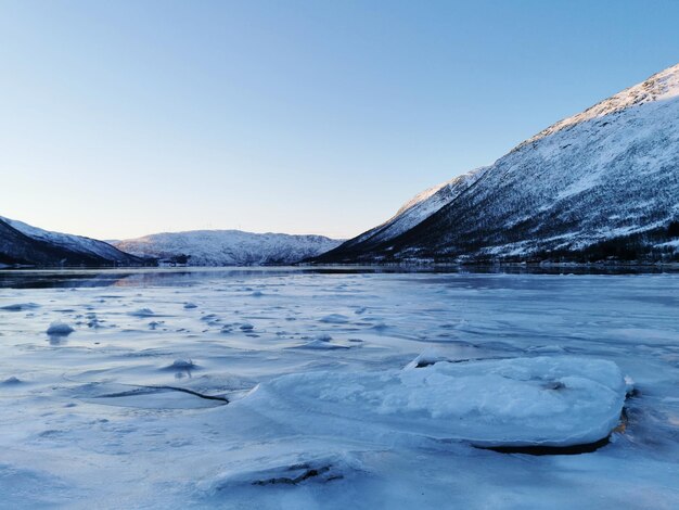 ノルウェーのカットフィヨルデンにある雪に覆われた丘のそばの凍った湖が日中に捕獲されました