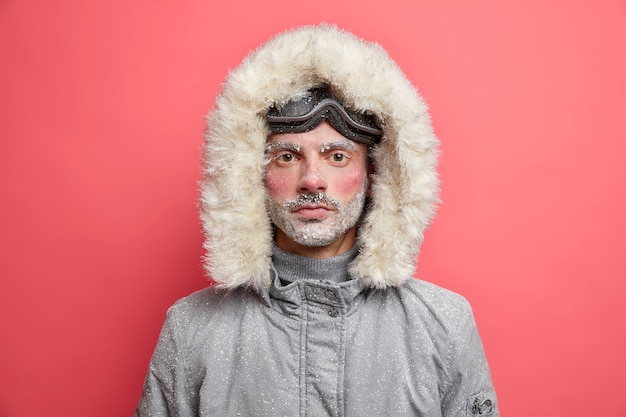 無料写真 雪に覆われた凍った無精ひげを生やした男は、フード付きの灰色のジャケットを着ています。