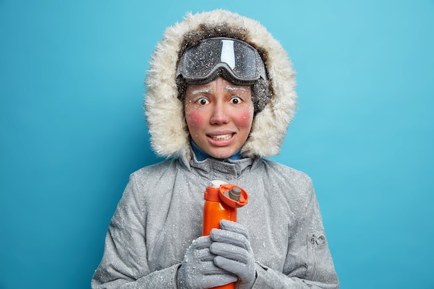 凍った女性が歯を食いしばり、寒さから震え、魔法瓶からの温かい飲み物で体を温めようとします。赤い頬のまつげが凍りつくような冬の時期に活発に休息します。