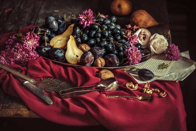 The fruit bowl with grapes and plums against a maroon tablecloth