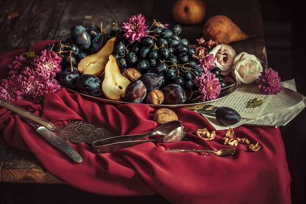 The fruit bowl with grapes and plums against a maroon tablecloth