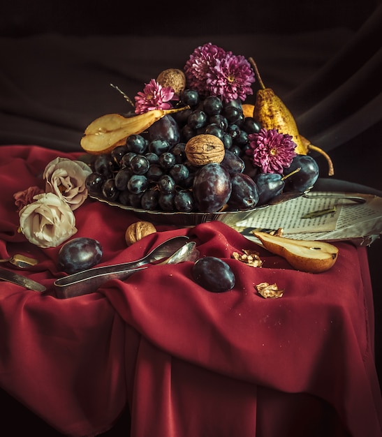 The fruit bowl with grapes and plums against a maroon tablecloth