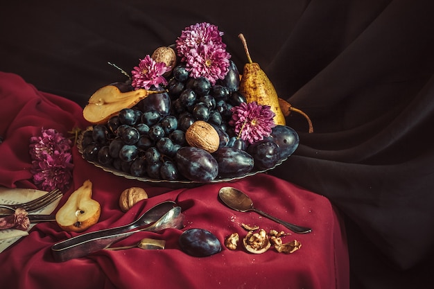 The fruit bowl with grapes and plums against a maroon tablecloth