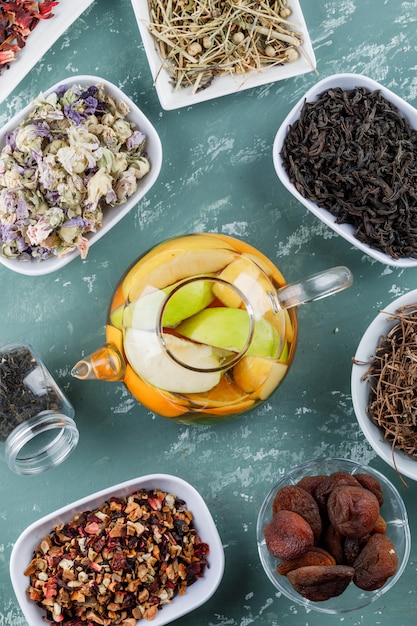 Fruit infused water in a teapot with dried apricots, herbs, cherry stalks top view on a plaster surface