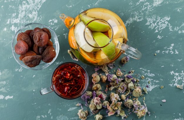 Acqua infusa di frutta in una teiera con albicocche secche, erbe aromatiche, vista dall'alto di tisana su una superficie di gesso