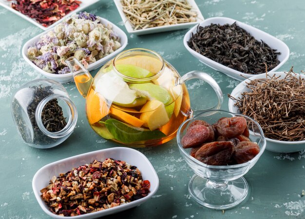 Fruit infused water with dried apricots, herbs, cherry stalks in a teapot on plaster surface