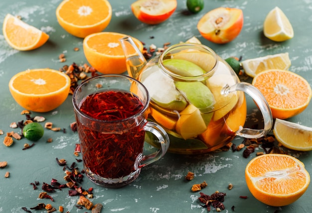 Фруктовая вода с травяным чаем, апельсинами, лимонами, лаймами в чайнике на гипсовой поверхности