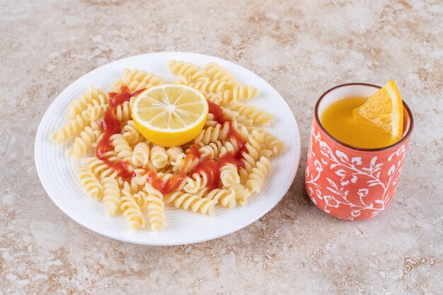 Fruit juice and macaroni platter with slices of lemon on marble surface.