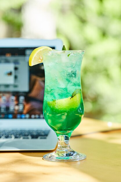 Free photo a fruit lemonade next to laptop on wooden table