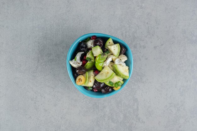 Fruit salad in a blue cup with black olives.