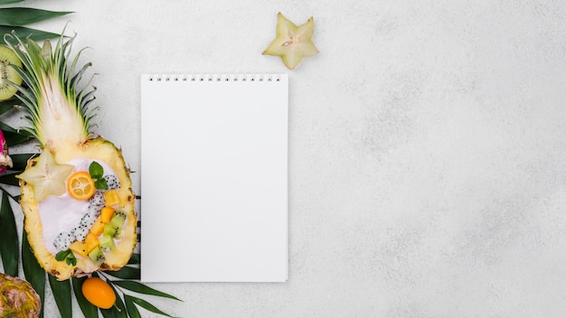 Fruit salad in half of pineapple with empty notepad