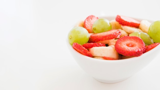 Fruit salad in white bowl isolated on white backdrop