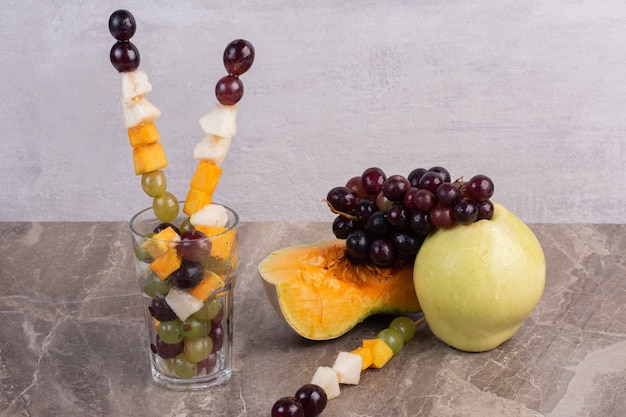 Fruit sticks and fresh fruits on marble surface.