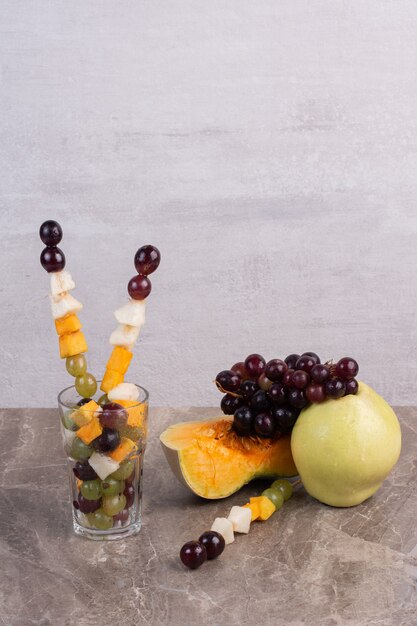 Фруктовые палочки и свежие фрукты на мраморной поверхности.