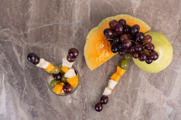 Fruit sticks and fresh fruits on marble surface.