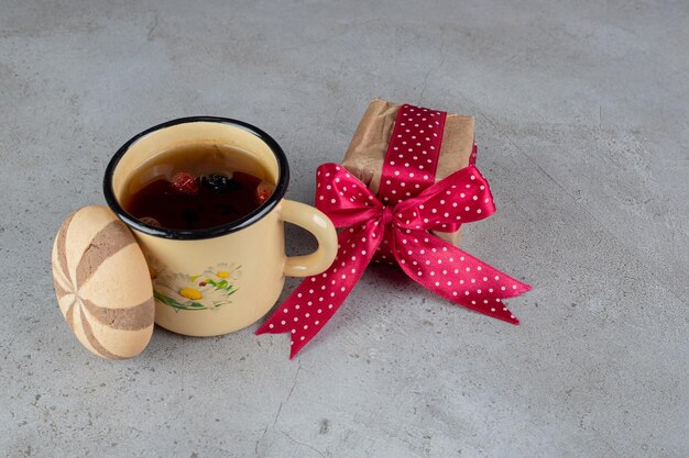 Fruit tea, a cookie and a gift package on marble surface.