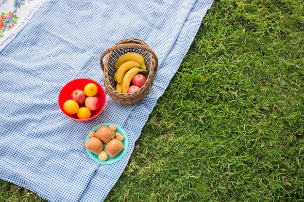 Free photo fruits basket and baked bread on blanket over the green grass