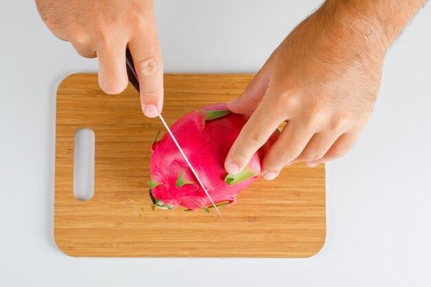 Fruits concept flat lay. hands cutting dragon fruit on wooden board.