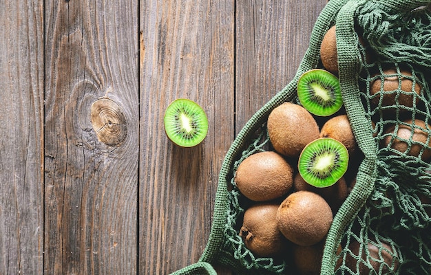Frutti di kiwi in una borsa a rete su uno stile rustico di vista superiore del fondo di legno