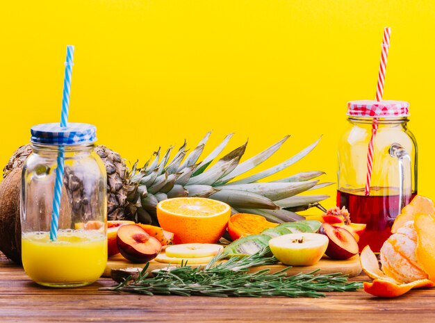 Fruits; rosemary and juice mason jar on chopping board against yellow backdrop