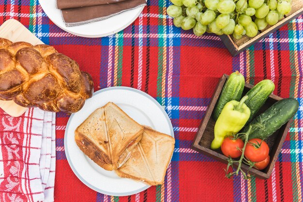 Fruits; sandwiches and baked braided bread loaf on checkered tablecloth