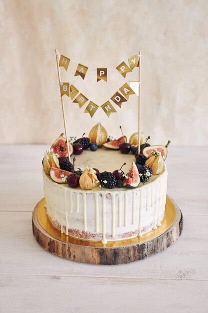 A fruity birthday cake with birthday topper, fruits on top and white drip on beige background