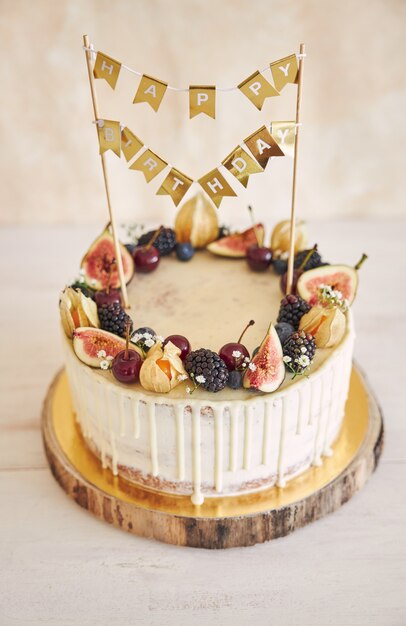 A fruity Birthday Cake with Birthday Topper, fruits on top and white drip