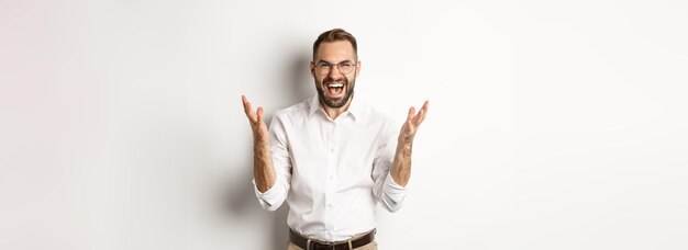 Frustrated and angry man screaming in rage shaking hands furious standing over white background