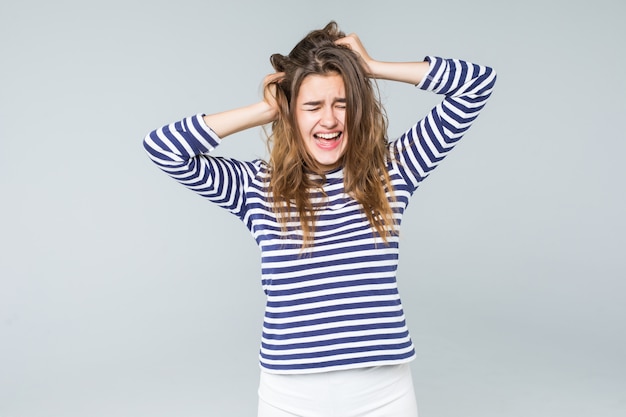 Free photo a frustrated and angry woman is screaming out loud and pulling her hair isolated on white background