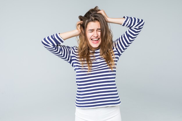 A frustrated and angry woman is screaming out loud and pulling her hair isolated on white background