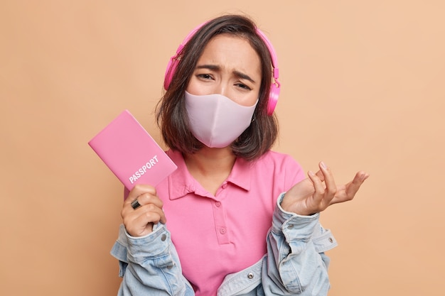 Frustrated Asian woman feels unhappy because cannot travel abroad wears protective hygiene mask against coronavirus wears casual clothes wants to have trip