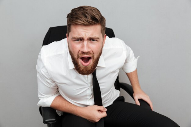 Frustrated bearded businessman sitting in chair and staring at