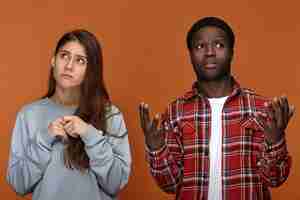 Free photo frustrated black dark-skinned guy wearing red plaid shirt shrugging shoulders and frowning, holding hands in front of him, don't understand his unhappy upset white girlfriend who is having periods