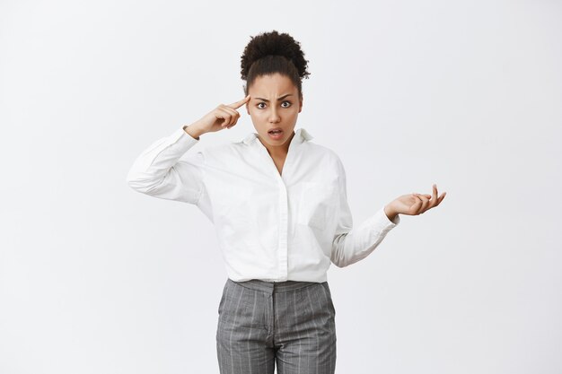 Frustrated and bothered african-american businesswoman pointing at head and scolding employee